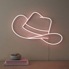 a neon sign with a hat on top of it next to a bowl and book