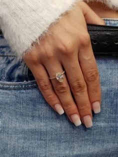 a woman's hand with a diamond ring on her left finger, wearing jeans and a white sweater