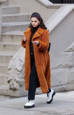 a woman is walking down the street wearing an orange coat and black pants with white sneakers