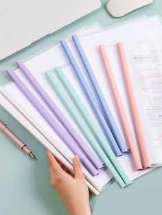 a person holding a pen next to several different colored pens on top of a desk