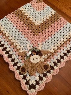 a crocheted blanket with a teddy bear on it sitting on a wooden floor