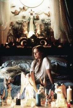 a woman sitting on top of a bed next to candles and figurines in front of her