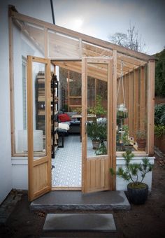 an open wooden door leading into a small room with plants in the window sill