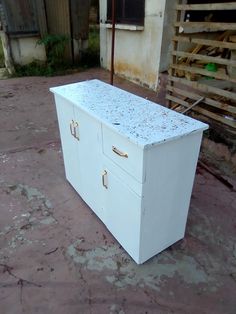 a white cabinet sitting on top of a cement floor next to a building and wooden fence