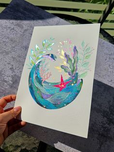 a person holding up a card with watercolors on it