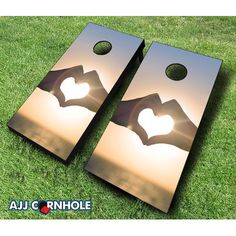 two metal cornhole game boards with the shape of a heart and hands making a gesture