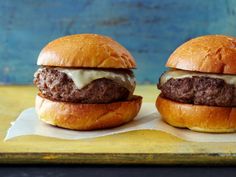 two hamburgers sitting on top of a cutting board next to each other, one with cheese and the other without