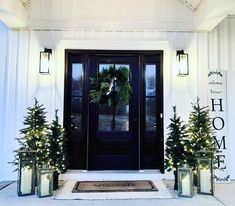 front door decorated for christmas with wreaths and evergreen trees on the doorstep, lit by lanterns