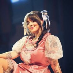 a woman in a pink dress with tattoos on her arm and leg, sitting down