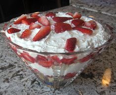 a dessert with strawberries on top in a glass bowl sitting on a countertop