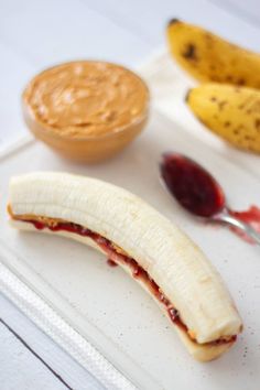 a banana sitting on top of a white plate with peanut butter and jelly in the background