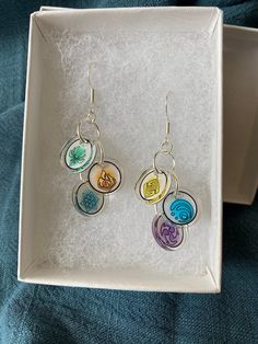 two pairs of earrings in a box on top of a blue cloth covered tablecloth