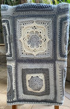 a crocheted blanket sitting on top of a wooden stand next to a potted plant