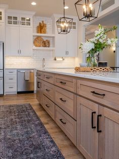 a kitchen with white cabinets and wood floors is lit by pendant lights above the island