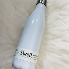 a stainless steel water bottle sitting on top of a white fur covered floor with the words swell written on it