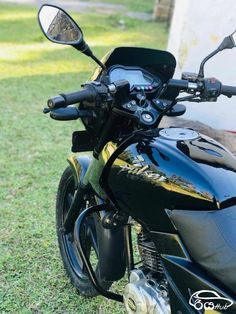 a black motorcycle parked on top of a lush green field next to a building and grass covered ground