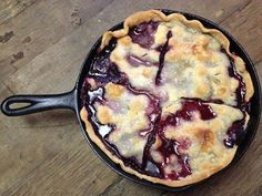 a pie sitting in a skillet on top of a wooden table next to a knife