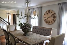 a dining room table with chairs and a large clock on the wall behind it,