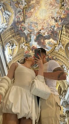 a man and woman taking pictures in front of a ceiling with paintings on the walls