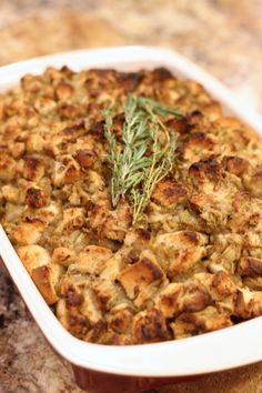 a casserole dish filled with stuffing and topped with a sprig of rosemary