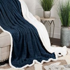 a blue blanket sitting on top of a couch next to a white chair and potted plant