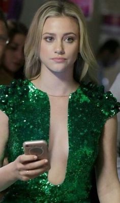 a woman in a green dress holding a cell phone and looking at the camera while people look on