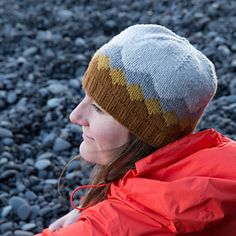 a woman wearing a red jacket and a gray hat sitting on top of a pile of rocks