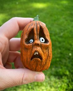 a hand holding a small carved pumpkin with eyes