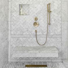 a bathroom with white marble and gold fixtures on the shower wall, along with a brass faucet