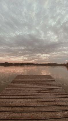 a wooden dock sitting on top of a lake under a cloudy sky