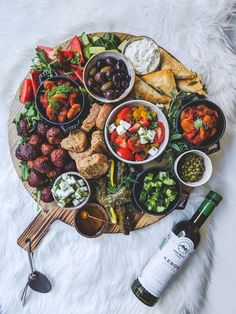 a platter filled with meats, vegetables and olives next to a bottle of wine