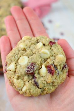 a hand holding a cookie with cranberries and white chocolate chips on it's side