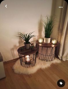 two small tables with plants on them in front of a white wall and wooden floor