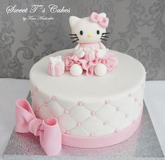 a hello kitty cake is decorated with pink and white icing, bows, and fondant