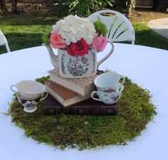 a tea pot with flowers on top of a book and two cups next to it