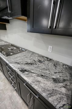 a kitchen counter top with black cabinets and marble flooring in the middle, next to an oven