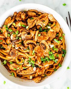 a white bowl filled with noodles and mushrooms on top of a marble table next to chopsticks