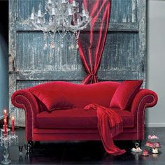 a red couch sitting next to a chandelier in front of a wooden door