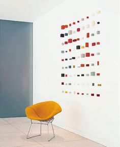 an orange chair sitting in front of a white wall with colorful squares on it's back