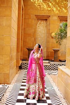 a woman in a pink and gold bridal outfit standing on a black and white checkered floor