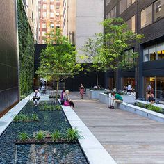 people are sitting on benches near a small pond in the middle of a city square