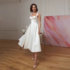 a woman in a white dress standing on a wooden floor next to a pink painting