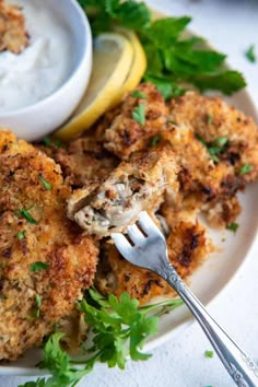 a white plate topped with chicken cutlets next to a bowl of ranch dressing and a fork