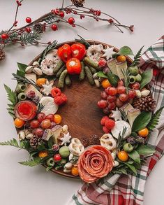 an arrangement of fruits and vegetables arranged in a wreath on a wooden platter next to a plaid napkin