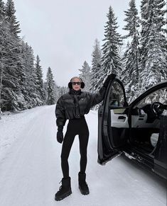 a woman standing in the snow next to a car with its door open and her hand out