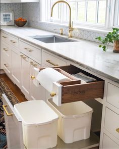 a kitchen with white cabinets and two bins on the bottom shelf that are open