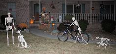 two skeletons on bikes in front of a house decorated for halloween