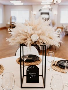 a centerpiece with feathers on top of a white table cloth and place cards in front of wine glasses