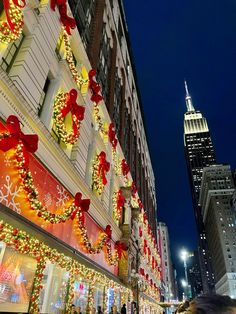 people are walking down the street in front of christmas decorations and lights on buildings at night