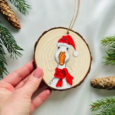 a hand holding a wooden ornament with a duck wearing a red hat and scarf